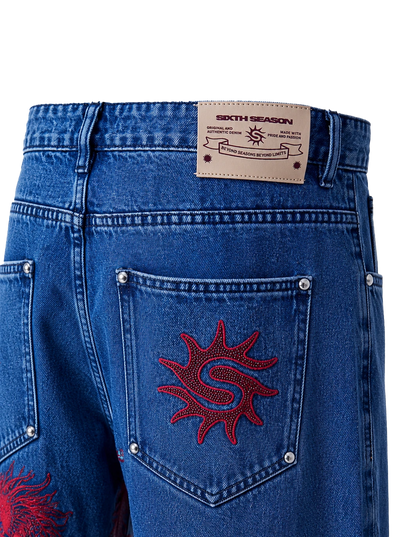 Close-up of the back waistband and pocket area of blue denim jeans. A tan leather patch at the back waist reads 'SIXTH SEASON'.